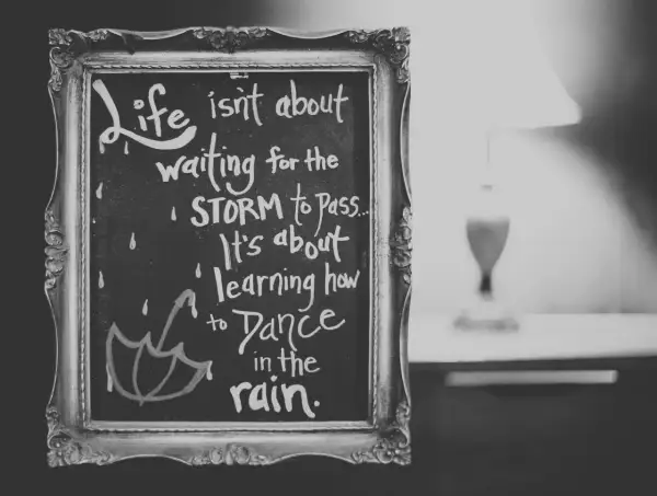 Czarno-biała tablica w ozdobnej ramie z inspirującymi cytatami po angielsku: "Life isn't about waiting for the storm to pass. It's about learning how to dance in the rain.