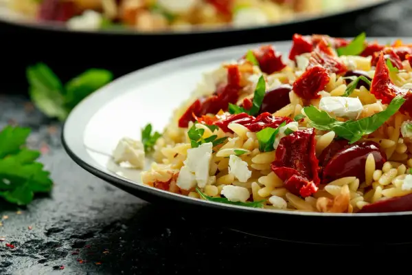 Salade de pâtes orzo avec tomates séchées, mozzarella fraîche et basilic. Un plat coloré et savoureux.