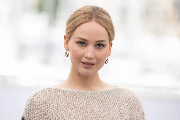 Jennifer Lawrence, gwiazda wielu filmów, w beżowym swetrze i złotych kolczykach.