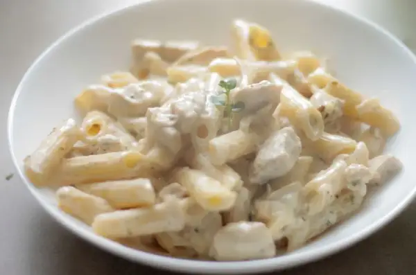 Penne z kurczakiem w kremowym sosie, udekorowane gałązką ziół. Pyszne danie, które zachwyci każdego smakosza makaronu z kurczakiem.