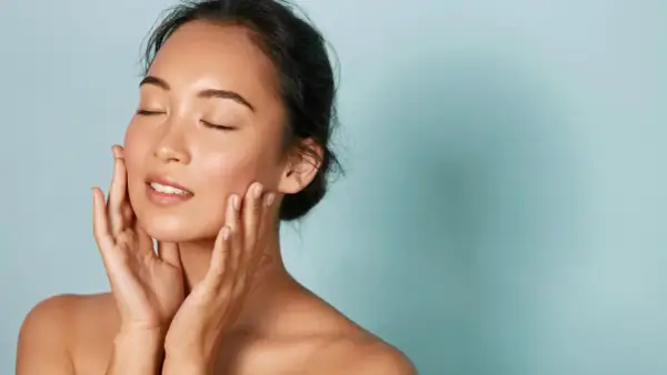 Donna con pelle luminosa e mani sul viso, un esempio di perché i coreani hanno la pelle perfetta.