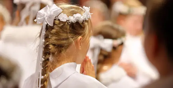 Dziewczynka w białej sukience i wianku modli się. To piękny widok, co na komunie.