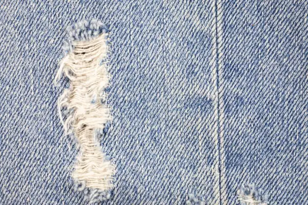 Zbliżenie na niebieski denim z przetarciami. Dowiedz się, jak zrobic przetarcia na dzinsach, by nadać im stylowy, znoszony wygląd.