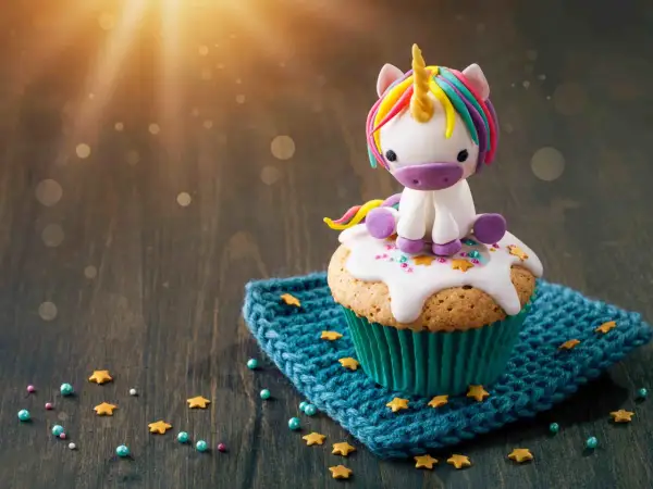 Un cupcake orné d'un adorable licorne en pâte à sucre, posé sur un glaçage blanc et des étoiles dorées. Le glaçage cupcake sucre glace est parfait pour une touche magique.