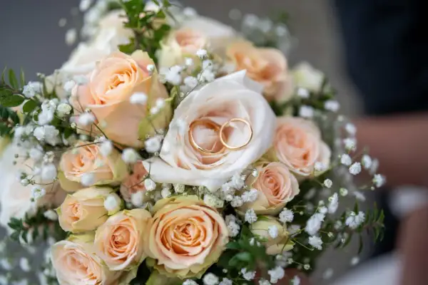 Ein Hochzeitsstrauß mit Pfirsichrosen und Schleierkraut, darin zwei goldene Ringe. Ein Symbol für 27 Jahre verheiratet.