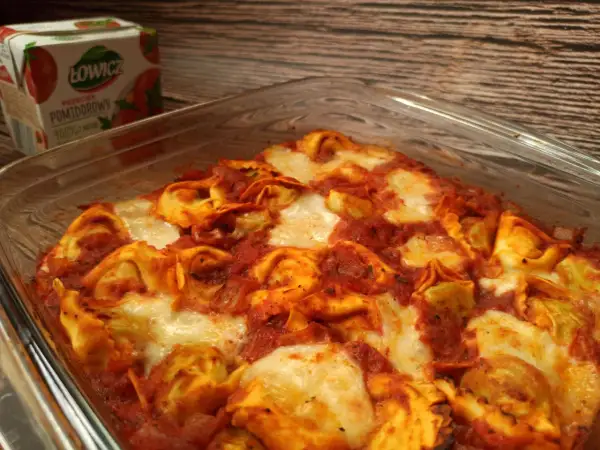 Pyszna zapiekanka z tortellini w sosie pomidorowym, zapieczona z serem. Obok kartonik przecieru pomidorowego Łowicz.