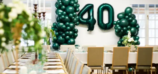 Uroczyste przyjęcie z okazji 40 urodzin. Zielone balony tworzą liczbę 40. Stół nakryty do eleganckiej kolacji.