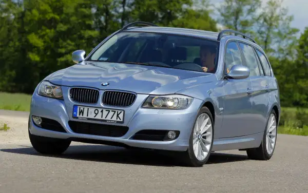 Błękitne BMW E91 na drodze, widać wyraźnie jego przednie światła i grill.
