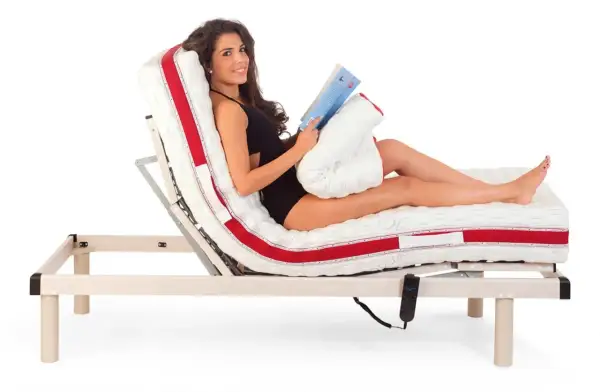 Donna sorridente legge un libro a letto, con il materasso regolabile che offre la postura corretta per guardare la TV o rilassarsi.