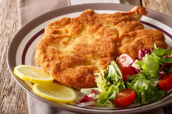 Chrupiący kotlet milanese z cytryną i świeżą sałatką z pomidorkami.