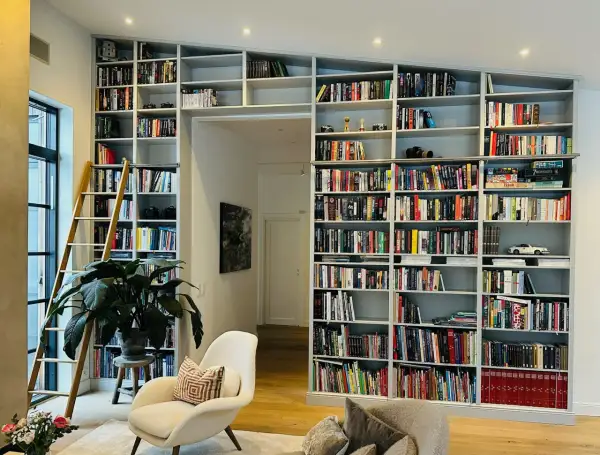 En stor inbyggd bokhylla med en stege, fylld med böcker och prydnadssaker. Perfekt inbyggd bokhylla inspiration för ett bibliotek.