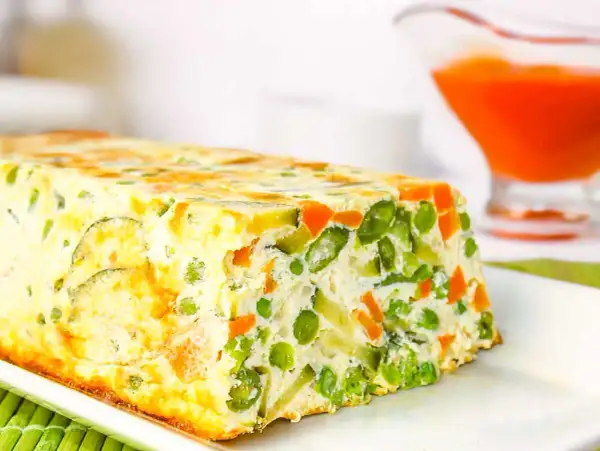Un delicioso pastel de verduras, con guisantes, zanahoria y calabacín, horneado en un molde rectangular.