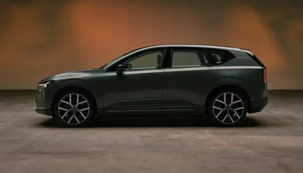Volvo EX60 gris oscuro, perfil lateral, con fondo degradado naranja y suelo de hormigón.
