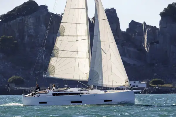 Un elegante catamarano solca acque azzurre, con vele bianche gonfie di vento, mentre sullo sfondo si stagliano scogliere rocciose.