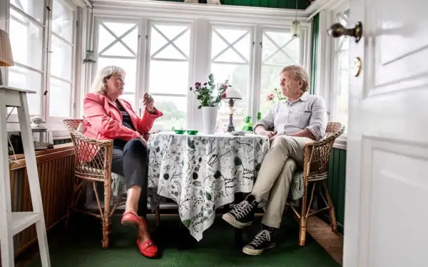 Britt Skogman och en man sitter vid ett bord i ett solrum.