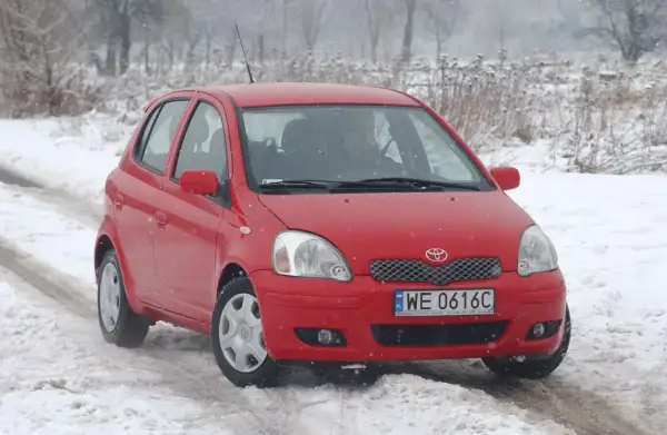Czerwona Toyota Yaris 1 na śniegu. Kierowca przygotowuje się do wymiany żarówki.