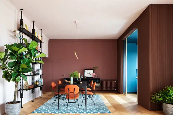 Un soggiorno moderno con pareti color mattone, sedie arancioni vivaci e un tappeto blu. Un esempio di come abbinare il color mattone con tocchi audaci.