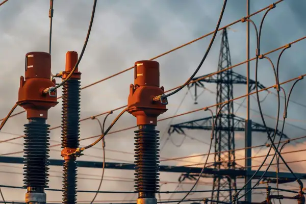 Trzy izolatory z brązowymi głowicami, przygotowane do dystrybucji energii. W tle widać wieżę przesyłową, symbolizującą napięcie fazowe a międzyfazowe.