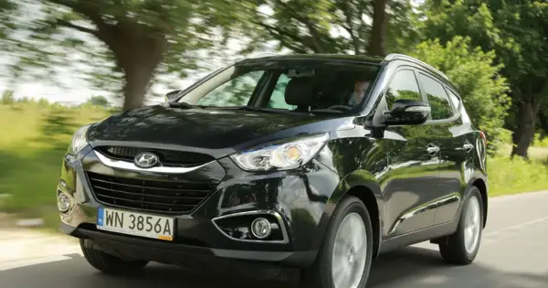 Czarny Hyundai ix35 2.0 benzyna w ruchu, z zielenią drzew w tle.