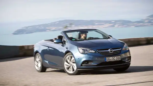 En blå Opel Cascada cabriolet kör längs en kustväg med havet i bakgrunden.
