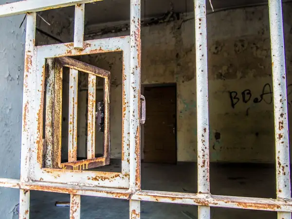 Grille rouillée d'une cellule abandonnée, porte ouverte. Un vestige de l'urbex à Laval, où le passé murmure.