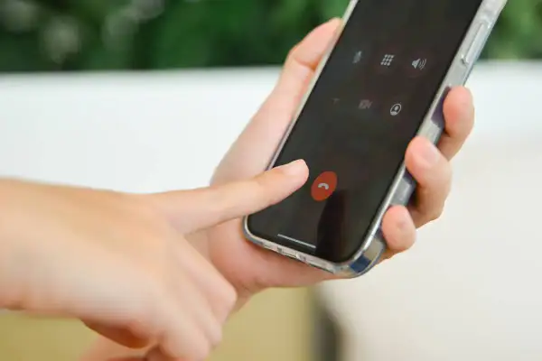 Dłoń naciska czerwony przycisk zakończenia rozmowy na ekranie smartfona, przypominając o kultowych dzwonkach na telefon.