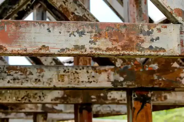Metalowe belki konstrukcji pokryte rdzą i łuszczącą się farbą. To przykład tego, co to jest korozja, niszcząca metal.