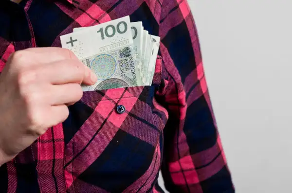 Ręka wkłada banknoty 100 zł do kieszeni koszuli w kratę. Może to symbolizować wynagrodzenie ryczałtowe.