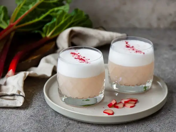 Två glas med rabarber sour, toppade med skum och strödd rabarberpulver. En härlig syrlig sommardröm.