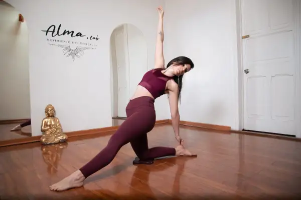 Mujer en postura de yoga, demostrando la fluidez del vinyasa yoga. Reflejo en espejo y Buda dorado.
