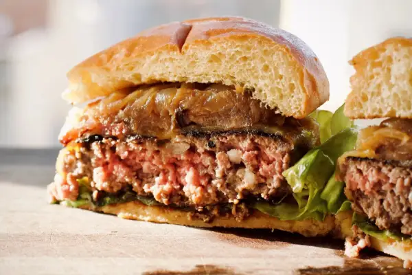 Przekrojony, soczysty burger z karmelizowaną cebulą i sałatą na desce.