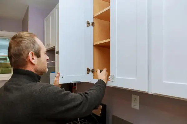 Hombre ajustando bisagras para como regular puertas de armario.