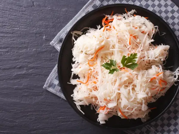 Ein Teller mit traditionellem Sauerkraut-Rezept, garniert mit Petersilie und Karottenstreifen, auf dunklem Stein serviert.
