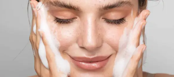 Visage de femme aux yeux fermés, profitant d'un nettoyage en profondeur avec de la mousse sur les joues.
