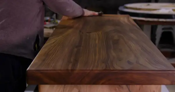 Main d'artisan polissant un plateau en bois exotique pour un entretien intérieur parfait.