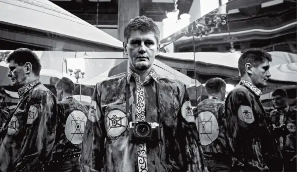 Krzysztof Miller w lustrzanym odbiciu, z aparatem na szyi, w koszuli z motywem oka.