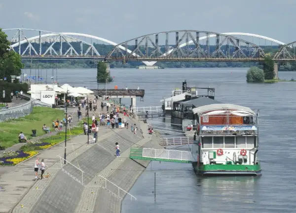 Toruń: Wisła, bulwar z ludźmi, restauracja na wodzie i mosty w tle.