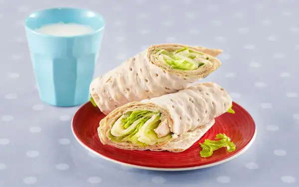 Två saftiga tonfisk wraps med krispig sallad på en röd tallrik, bredvid ett glas mjölk.