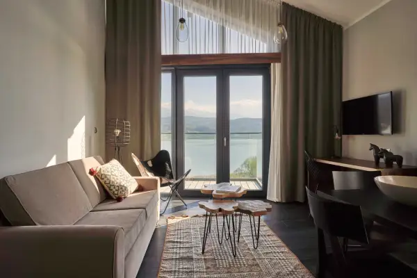 Przytulny pokój z widokiem na jezioro w hotelu Lake Hill Resort & Spa w Karkonoszach. Sofa, stoliki kawowe i krzesło motylkowe tworzą komfortową przestrzeń.