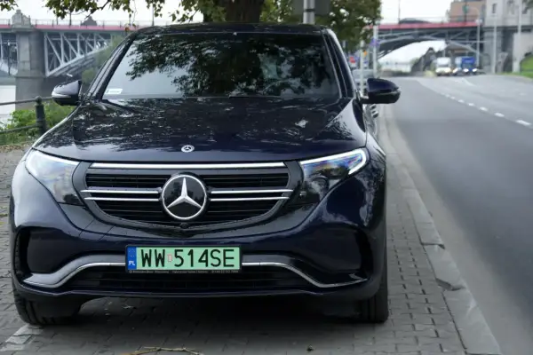 Ciemnoniebieski Mercedes EQC z tablicą rejestracyjną WW 514SE zaparkowany przy ulicy, w tle most.