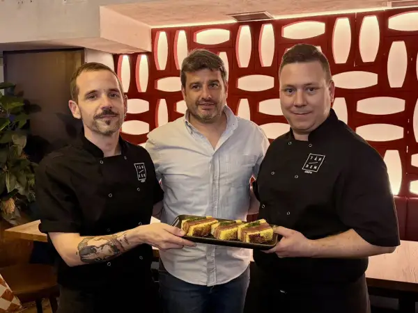 Tres hombres sonríen mientras uno sostiene una bandeja con aperitivos. ¡Un buen lugar donde comer en el Actur!
