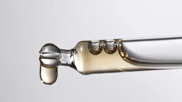 Tropfen eines goldenen Serums, das Bisabolol enthält, fallen aus einer Pipette.