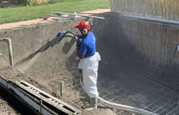 Un ouvrier projette du béton pour créer un bassin en béton étanche. La structure métallique est visible.