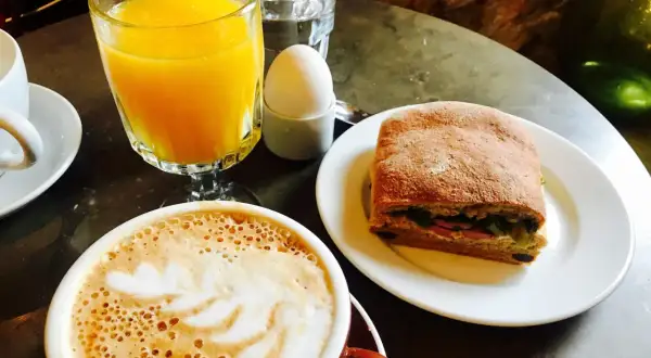 En kopp kaffe med lattekonst, apelsinjuice, ett kokt ägg och en macka. En perfekt frukost som ger en känsla av comfort food.