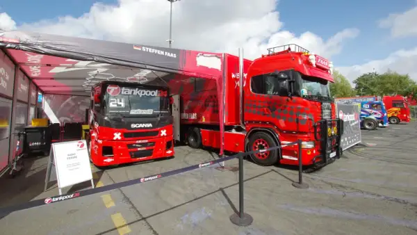 Deux camions de course rouges, prêts pour la vitesse max, sont garés sous une tente. L'un porte le numéro 24.