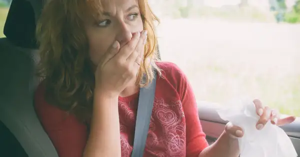Kobieta w samochodzie zakrywa usta, czując mdłości. Może to być skutek choroby lokomocyjnej, na którą pomaga difenhydramina.