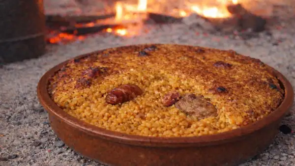 Arroz con costra recién hecho, con trozos de carne y salchicha, cocinándose a la leña.