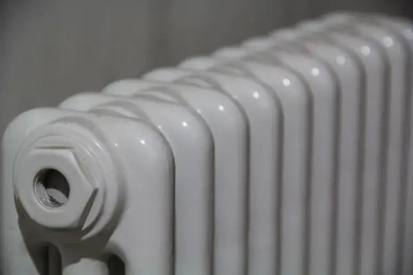 Radiador de mica blanco, con sus aletas curvas y un detalle de conexión en un extremo.