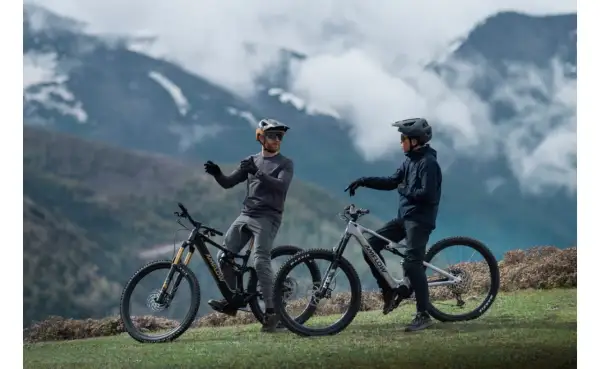 Dos ciclistas con cascos y bicicletas ebike en un paisaje montañoso, listos para explorar nuevas rutas.