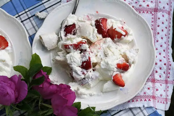 En härlig Eton Mess med färska jordgubbar och marängbitar, serverad på en vit tallrik med en vacker duk och rosor.